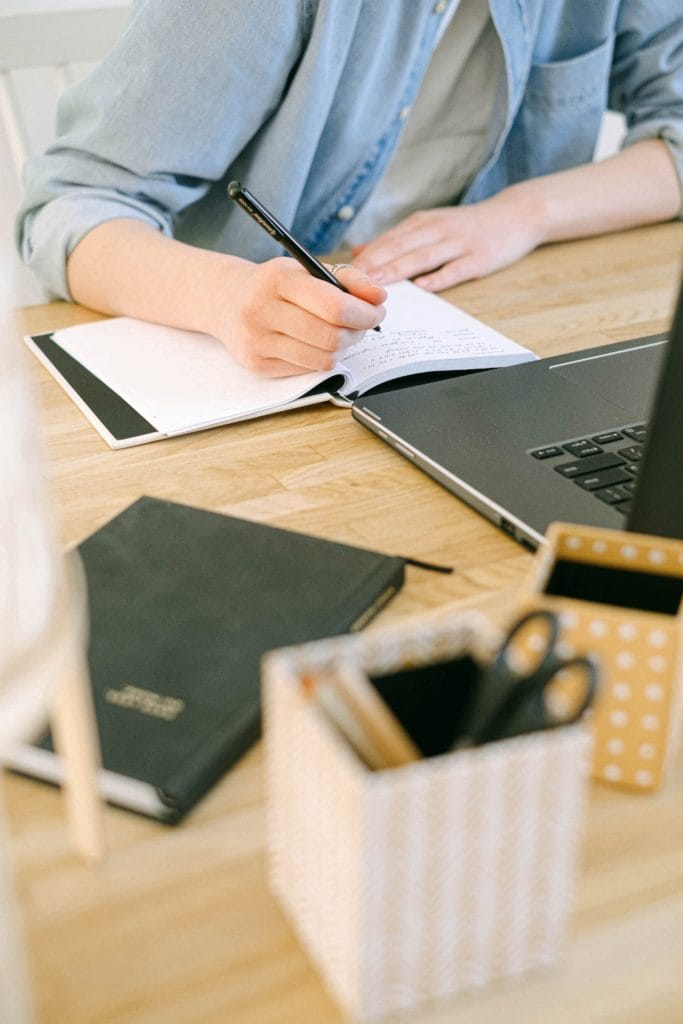 Person writing in a notepad whilst looking at a laptop