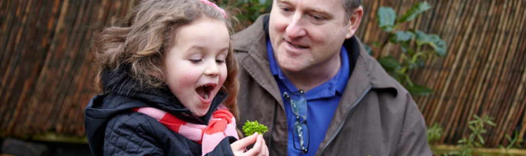 Dad with daughter as she looks at a leaf in amazement